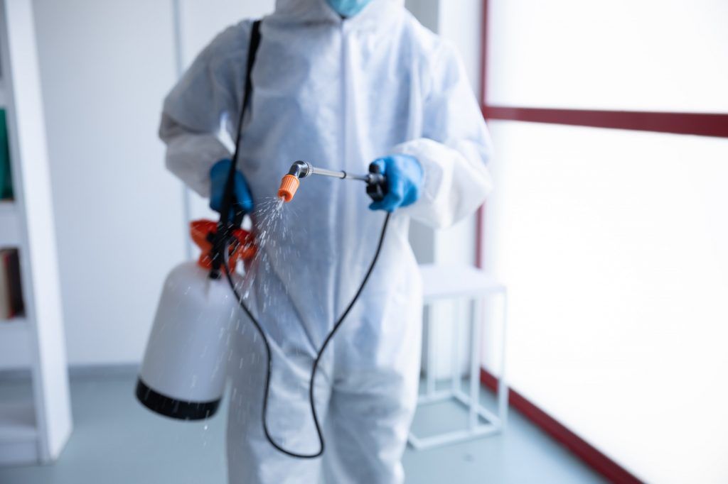 mid section of health worker wearing protective clothes cleaning using disinfectant